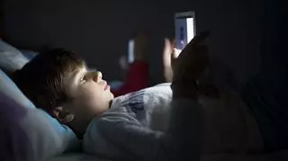 Chłopiec leżący w łóżku trzymający tablet