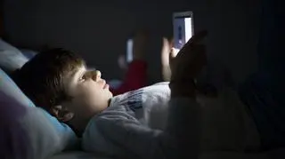 Chłopiec leżący w łóżku trzymający tablet