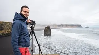 Mężczyzna stoi przy statywie z aparatem nad morzem