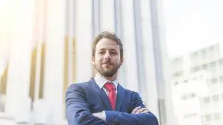 Atrakcyjny młody biznesmen stoi na tle budynku.