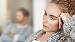 Smutna kobieta, w tle siedzi mężczyzna