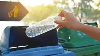 Ręka wrzucająca plastikową butelkę do kosza na śmieci