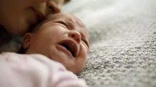 Płaczące niemowlę. Matka całuje dziecko w główkę. 