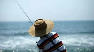 człowiek łowiący ryby nad morzem w kapeluszu 
