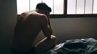 Zalamany mężczyzna z twarzą w dłoniach siedzi na łóżku, problemy z potencją