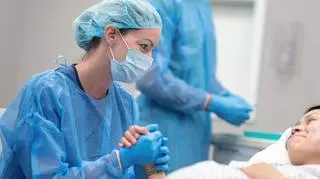 pielęgniarka trzyma za rękę rodzącą kobietę, nacinanie krocza przy porodzie
