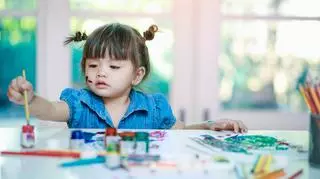 Dziewczynka siedzi przy biurku i maluje farbami