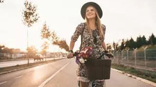 Kobieta jadąca na rowerze w kapeluszu i kwiecistej sukience