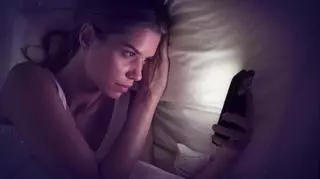 Młoda kobieta leży w łóżku i patrzy w smartfon