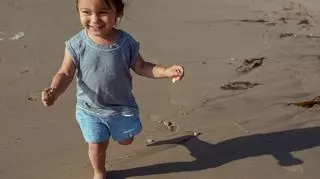 Mała dziewczynka w szortach biegnie po plaży