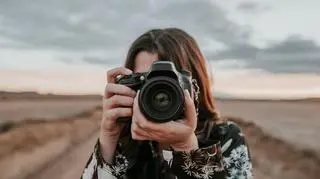 Kobieta z aparatem fotograficznym stoi na tle przyrody.
