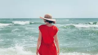 mloda kobieta na plazy w kapeluszu w czerwonej sukience morze fale lato moda