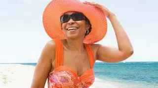 Uśmiechnięta kobieta po 50-tce w pomarańczowym kostiumie kąpielowym i dopasowanym kolorystycznie kapeluszu
