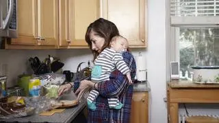 Zmęczona matka z niemowlakiem na ramieniu szykuje jedzenie w kuchni
