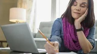 Kobieta siedzi przed laptopem i notuje.