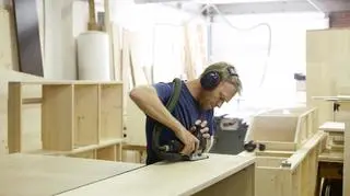 Młody mężczyzna szlifuje drewno w warsztacie