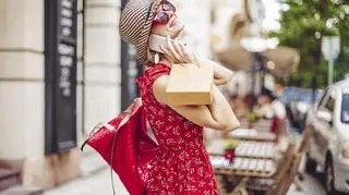 Modna kobieta w mieście ubrana w zwiewną czerwoną sukienkę odwraca się do kamery.