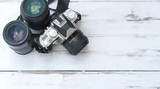 Aparat fotograficzny z akcesoriami leży na drewnianej podłodze. 