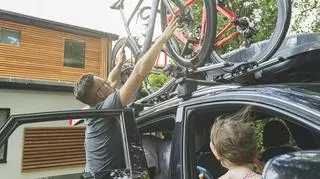 Bagażnik rowerowy na dach - mężczyzna montuje rowery na dachu samochodu.