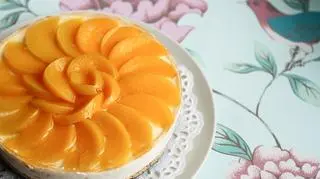 Sernik z brzoskwiniami ułożonymi na górze ciasta. 