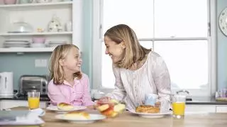 Mama z córką uśmiechają się do siebie jedząc śniadanie