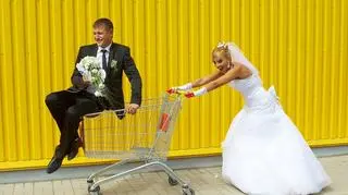 Para młoda bawi sie sklepowym wózkiem przed supermarketem