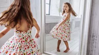 Mała dziewczynka w sukience przegląda się przed lustrem. 