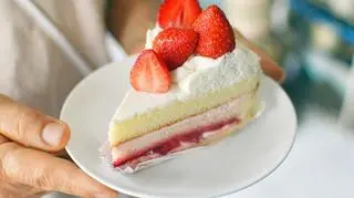 Kobieta, która trzyma talerz z kawałkiem tortu truskawkowego 