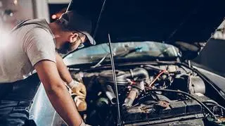 Mężczyzna w rękawicach oparty o auto przygląda się silnikowi