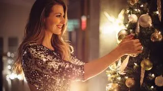 Kobieta w świątecznej sukience ubiera choinkę. Magia świąt.