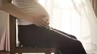 Kobieta w ciąży siedzi na krześle i trzyma się za brzuch