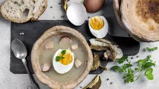 Żurek z jajkiem i kiełbasą w chlebie, obok jajka, zioła, grzyby, chleb