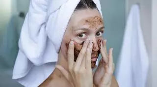 kobieta w białym ręczniku na głowie nakłada peeling kawowy na twarz