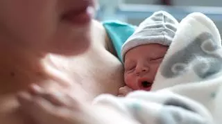 Kobieta po porodzie leży na łózku i przytula nowonarodzone dziecko