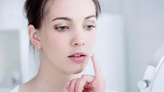 mloda kobieta przed lusterkiem naklada masc na twarz usta