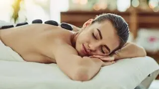 kobieta lezy w salonie kosmetycznym na masazu usmiecha sie na plecach ma ulozone gorace kamienie