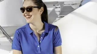 Kobieta w niebieskiej koszulce polo i okularach przeciwsłonecznych. 