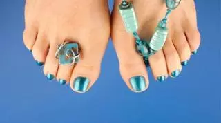 Stopy ozdobione turkusową biżuterią, z paznokciami pomalowanymi metalicznym, turkusowym lakierem.