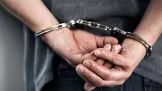 męskie dłonie zakute w kajdanki na plecach