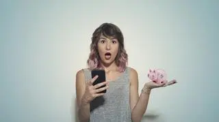 Zaskoczona kobieta z telefonem i świnka skarbonką