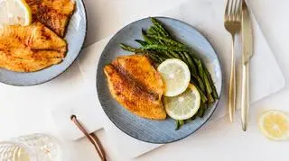 Tilapia smażona na talerzu ze szparagami i cytryną