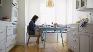 Kobieta pracuje w domu, siedzi przy stole w kuchni przy komputerze