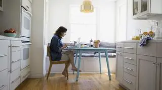 Kobieta pracuje w domu, siedzi przy stole w kuchni przy komputerze