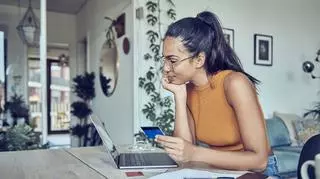 Młoda kobieta w okularach z kartą kredytową przy komputerze liczy rrso