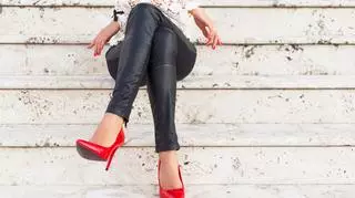 Kobieta w czarnych spodanich i czerwonych szpilkach siedzi na schodach
