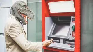 Mężczyzna w masce dinozaura wypłaca pieniądze z bankomatu