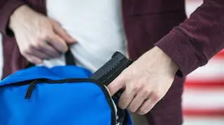Uczeń chowający pistolet w plecaku