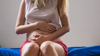 kobieta w ciazy siedzi na lozku obejmuje rekami brzuch