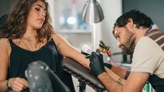 Mężczyzna robi kobiecie tatuaż na lewym przedramieniu