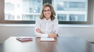 Uśmiechnięta kobieta w okularach, businesswoman, siedzi za biurkiem.